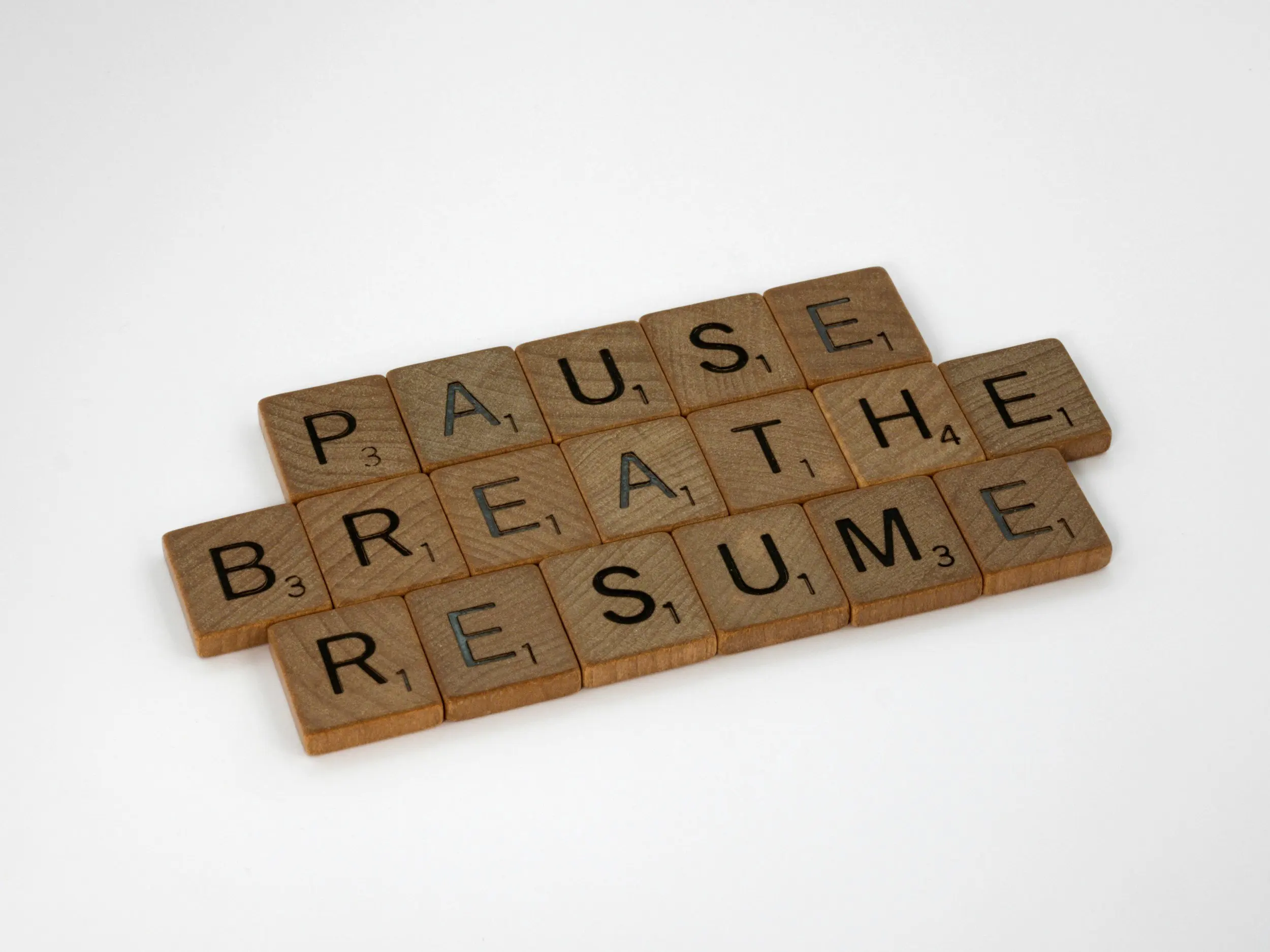 Scrabble tiles spelling out "PAUSE BREATHE RESUME" arranged on a white background, promoting mindfulness and reflection.